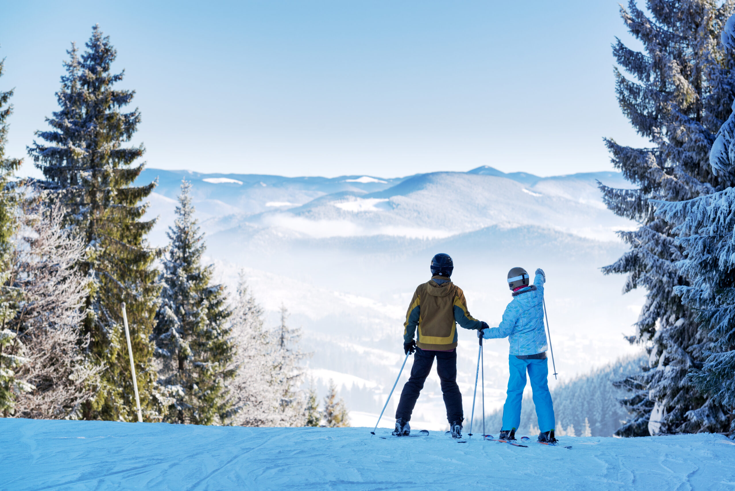 Twee skiërs kijken naar besneeuwde bergen onder een heldere hemel.